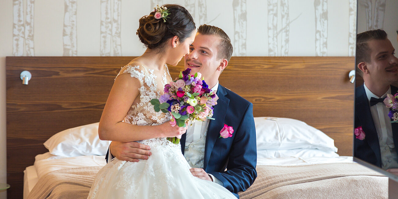 Hochzeitspaar sieht sich verliebt an und sitzt auf dem Bett